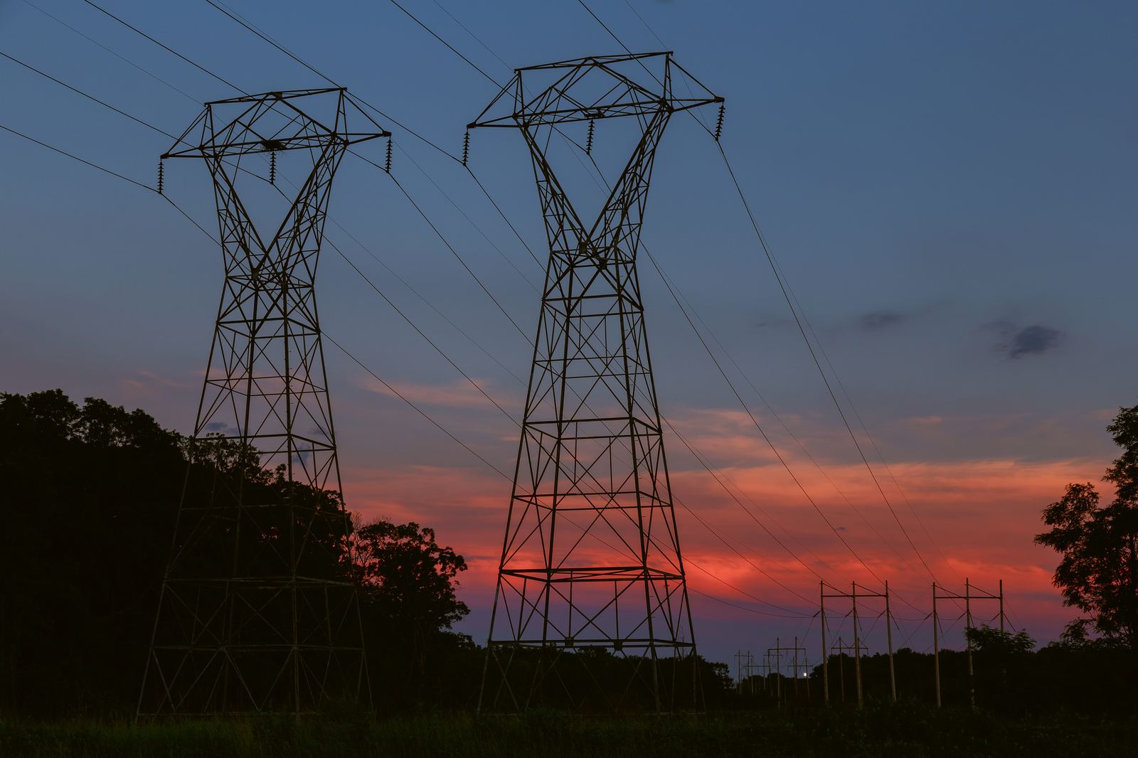 High-voltage electricity transmission towers silhouetted against a sunset sky