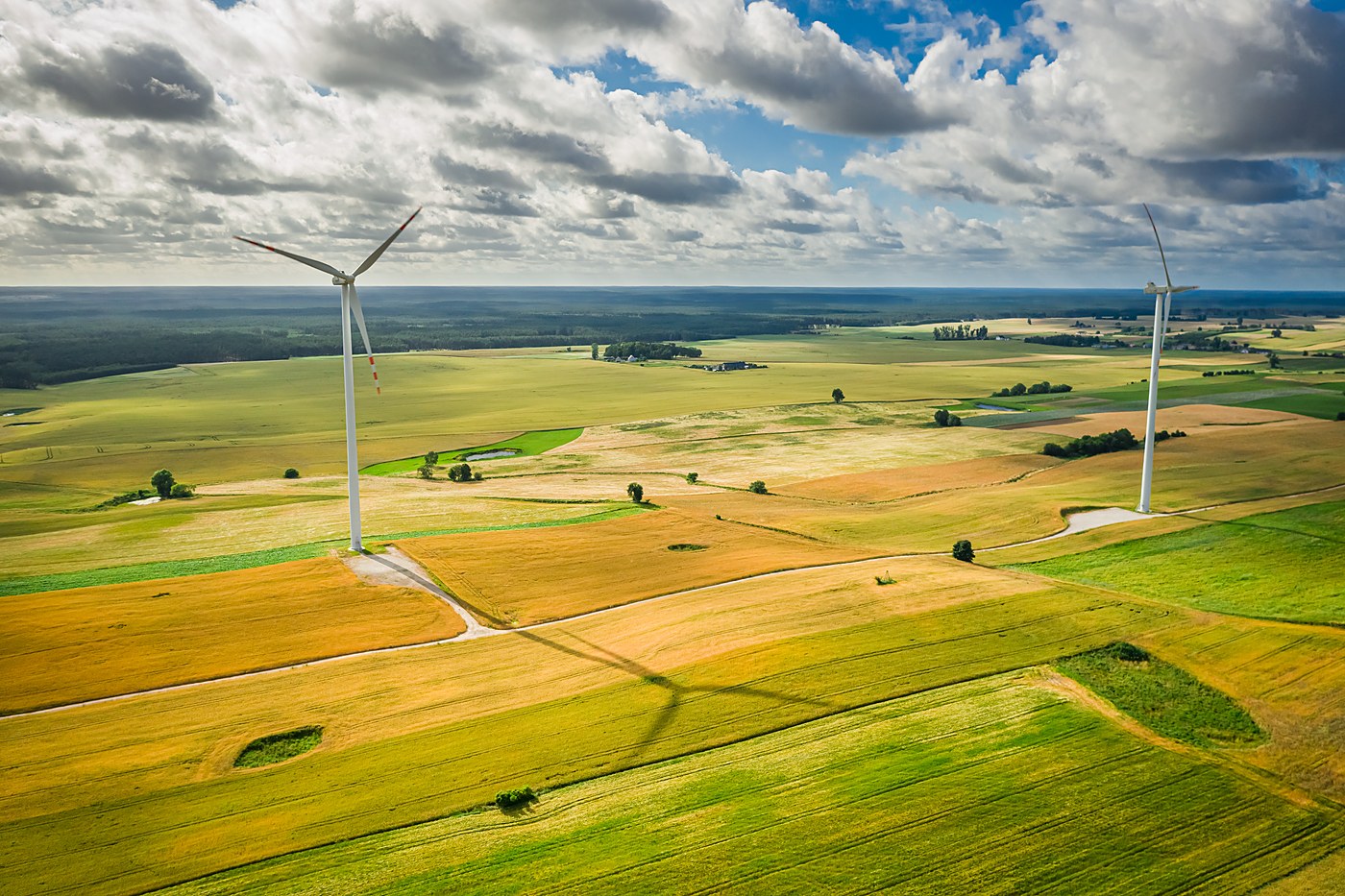 Aerial view of two wind turbines standing over farmland under a partly cloudy sky